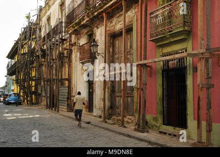 Ein Mann Spaziergänge entlang einer Straße in der Altstadt von Havanna, Kuba, vorbei an alten, unrestaurierten Gebäude mit Balkonen und hölzernen Gerüst befestigt. Stockfoto