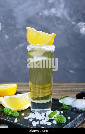 Mexikanische Gold Tequila in das Schnapsglas mit Zitronensaft und Meersalz auf dunklen Tisch. Retro Style, vintage. Stockfoto