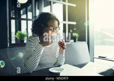 Lächelnde junge afrikanische Frau sitzt mit ihren Augen in einem Café geschlossen das Aroma von frischen Kaffee genießen. Stockfoto