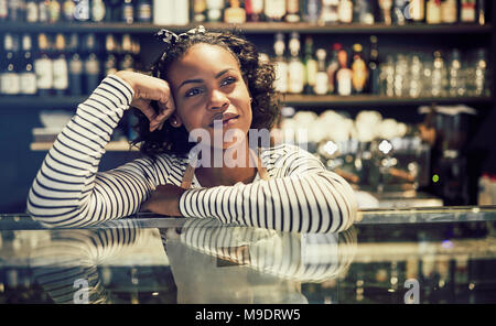 Lächelnden jungen afrikanischen cafe Eigentümer tief in Gedanken, während sich auf der Zähler von ihr angesagten Cafes Stockfoto