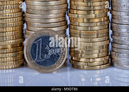 Eine 1 Euro Münze vor vielen mehr Münzen in Spalten auf weißem Hintergrund gestapelt mit Reflexion unten. Stockfoto