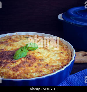 Hausgemachte leckere französische Quiche Lorraine Pastete vom Huhn, Pilzen und Brokkoli mit Basilikum in Blau runde Backen Form auf Holz- Hintergrund. Platz. Sel Stockfoto