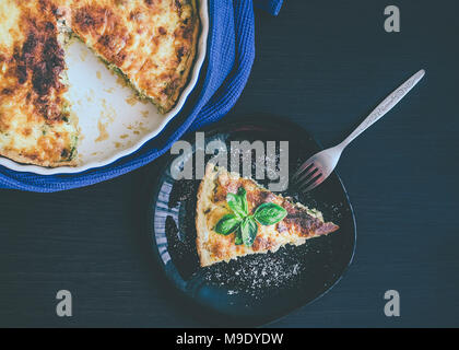 Quiche Lorraine Pastete mit Huhn, Pilze und Brokkoli in Blau runde Backen Form auf Holz- Hintergrund. Ein Stück französische Quiche Lorraine auf der Plat Stockfoto
