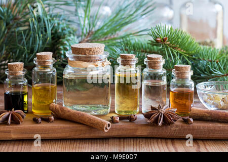 Auswahl von ätherischen Ölen mit Fichte und Kiefer Niederlassungen auf einer hölzernen Hintergrund, mit weihnachtlichen Gewürzen und Zutaten in den Vordergrund: Zimt, c Stockfoto