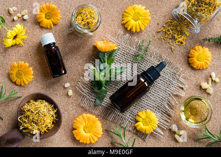 Zwei Flaschen Öl, calendula (Ringelblume), Thymian, Rosmarin und Weihrauch auf braunem Grund, Ansicht von oben Stockfoto