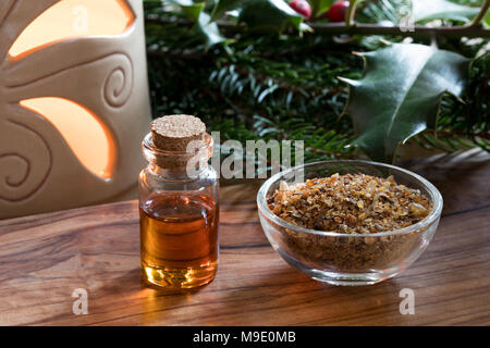 Eine Flasche Myrrhe ätherisches Öl Myrrhe Harz in eine Glasflasche und Zweige Fichte, Holly, Zweige und eine Aroma Lampe im Hintergrund Stockfoto