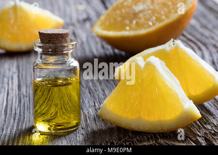 Eine Flasche orange ätherisches Öl auf einem Holztisch, mit frischen Orangen im Hintergrund Stockfoto