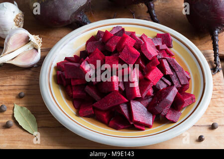 Vorbereitung von fermentierten Rüben - rote Bete in Scheiben auf den Teller, mit ganzen Rüben, Zwiebeln, Knoblauch und Gewürzen im Hintergrund Stockfoto