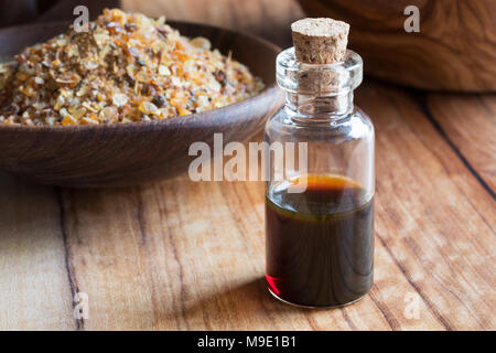 Eine Flasche Myrrhe ätherisches Öl auf einem Holztisch, mit Myrrhe Harz im Hintergrund Stockfoto