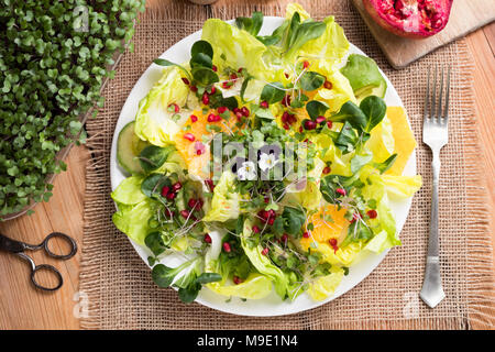 Gemüsesalat mit frisch gewachsen Grünkohl und Brokkoli microgreens, Kopfsalat, Feldsalat, Avocado-, Orangen-, Granatapfel- und edibe Blumen. Ansicht von oben. Stockfoto