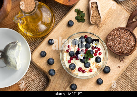 Hüttenkäse Gemischt mit Leinsamen öl, mit frischen Blaubeeren überstieg, gefroren wilde Preiselbeeren, essbare Blumen und Boden Leinsamen Stockfoto