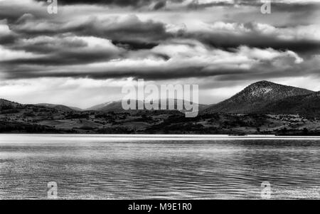 Schneebedeckten Gipfeln der schneebedeckten Berge wachsen über der Oberfläche von Jindabyne See während des Kalten stürmischen Winter Saison mit schweren Wolken, die gesamte Regio Stockfoto