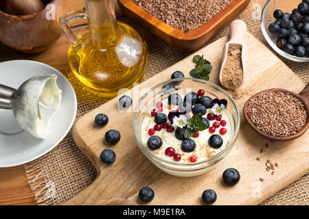 Hüttenkäse Gemischt mit Leinsamen öl, mit frischen Blaubeeren überstieg, gefroren wilde Preiselbeeren, Blumen und Boden Leinsamen Stockfoto