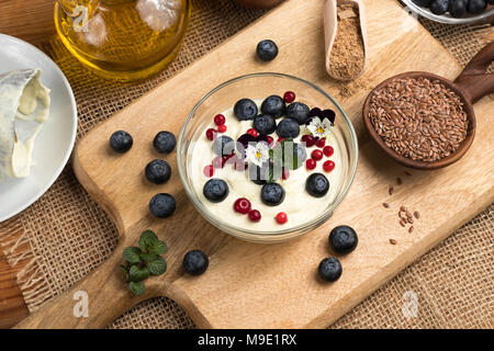 Hüttenkäse Gemischt mit Leinsamen öl, mit frischen Blaubeeren überstieg, gefroren wild Preiselbeeren und essbaren Blüten, mit ganzen und Boden Leinsamen Stockfoto