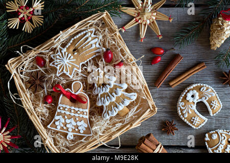 Dekoriert Weihnachten Lebkuchen Cookies in einem quadratischen Weidenkorb auf einen hölzernen Tisch, mit Stroh Ornamente, Zimt, Sternanis und Hagebutten in der b Stockfoto