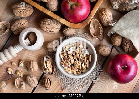 Und ohne Schale Walnüsse ohne Schale auf einem Holztisch, mit Äpfeln und einem Nussknacker im Hintergrund. Ansicht von oben. Stockfoto