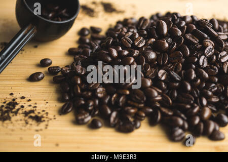 Messlöffel und verschüttete Kaffeebohnen auf Holzbrett. Stockfoto