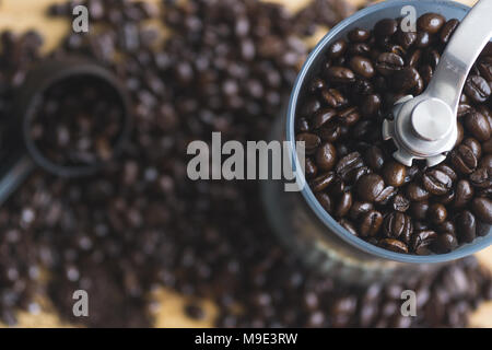 Manuelle Kaffeemühle und Messlöffel mit verschüttetem Kaffee Bohnen auf Holzbrett. Stockfoto