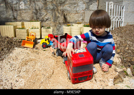 Wenig drei Jahre alten Jungen spielen im Sand mit einem Bagger und Kipper. Stockfoto