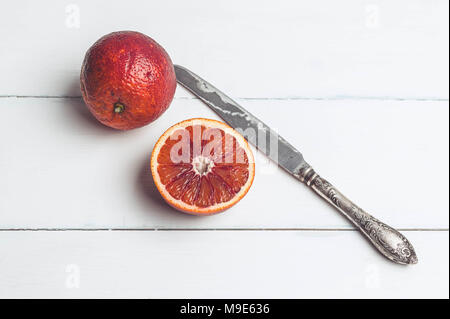 Blutorangen und Messer auf einem weißen Holz- Hintergrund. Saisonale Zitrusfrüchte Stockfoto