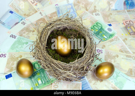 Goldene Ei im Nest und zwei andere goldene Eier auf einem Bett von Geld. Stockfoto