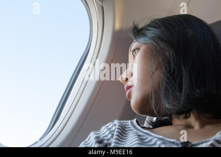 Eine junge Frau, die das Fliegen mit dem Flugzeug. Der Fluggast ist Blick aus dem Fenster eines fliegenden Flugzeugs. Stockfoto