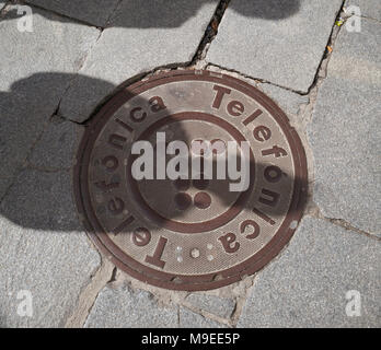 Schatten über Gusseisen Schachtdeckel mit Telefónica Logo und Namen in Pflaster Stockfoto