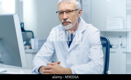 Erfahrene Grauhaariger Leitender Arzt schaut in die Kamera. Portraitfotos in der modernen und hellen Büro. Stockfoto