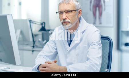 Erfahrene Grauhaariger Leitender Arzt schaut in die Kamera. Portraitfotos in der modernen und hellen Büro. Stockfoto