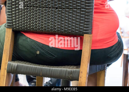 Der hintere Teil der fetten Körper auf einem Stuhl sitzen. Die Details der übergewichtige Person. Ein fetter Mann sitzt auf Stuhl in einem Restaurant. Stockfoto