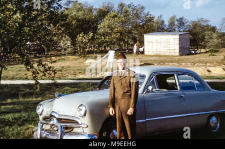 Junger Mann mit Brille in Militäruniform während des US-Wehrdienstes neben einer Ford-Limousine von 1949 in Fort Dix, New Jersey, USA in den 1950er Jahren Stockfoto