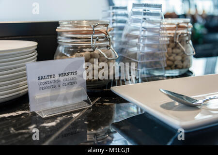 Gläser gesalzene Erdnüsse mit einem Schild Warnung abouit Sellerie, Erdnüssen und Gluten allergene Zutaten auf einem Airport Business Lounge Hotel Bar. Stockfoto