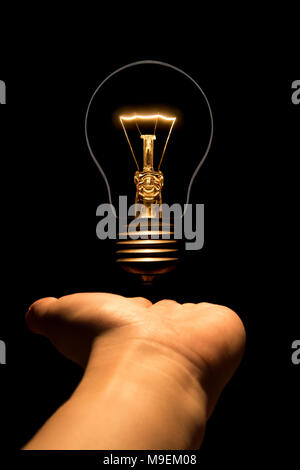 Hand, die eine Glühlampe auf schwarzem Hintergrund. Die Glühbirne als Symbol für eine Idee. Glühende tungsten Birne. Ökologische Konzept. Stockfoto