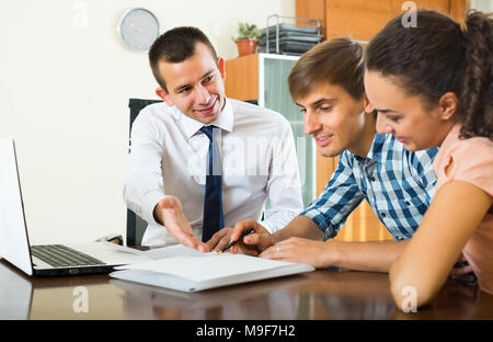 Positive agent diskutiert mit jungen Paar Details des Vertrags im Büro Stockfoto