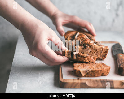 Butter, Zucker-freien Bananenbrot mit Hafermehl, weiche Quark, Honig. Frau hand mit Scheibe Bananenbrot auf grau Tabelle. Ideen Rezept gesunde Ernährung Frühstück. Selektiver Fokus Stockfoto