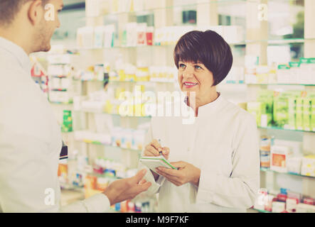 Fröhliche positive Frau Apotheker im weißen Mantel Kunden los im Drug Store zu finden Stockfoto