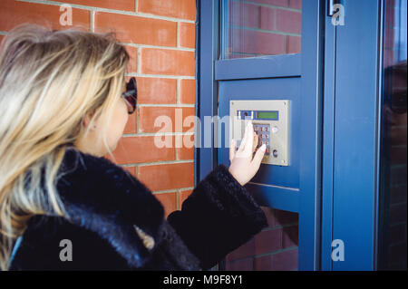 Junge blonde Frau in einem Pelzmantel, wählt den Code auf der Türsprechanlage Panel, drückt die Tasten mit den Fingern im Haus zu erhalten Stockfoto