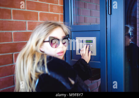 Junge blonde Frau in einem Pelzmantel, wählt den Code auf der Türsprechanlage Panel, drückt die Tasten mit den Fingern im Haus zu erhalten Stockfoto