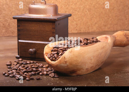 Kaffeebohnen in eine hölzerne Schaufel und Kaffeemühle auf dunklen Tisch aus Stein. Stockfoto