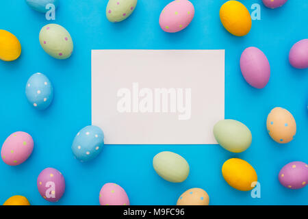 Ostern traditionelle Objekte auf blauem Hintergrund weißes Blatt Papier, umgeben von bunten Eiern isoliert Stockfoto