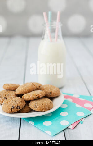 Glutenfreie Chocolate Chip Cookies mit einer Flasche Milch auf einem weißen Holz Hintergrund. Stockfoto
