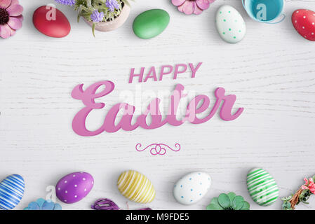 Frohe Ostern 3D-Text auf weißem Schreibtisch aus Holz mit Ostern bunte Eier und Blumen umgeben. Stockfoto
