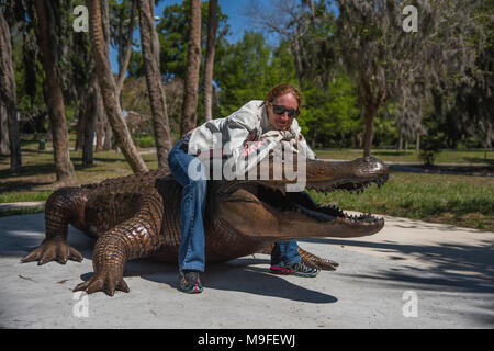 Hübschen roten Kopf Mädchen mit Sonnenbrille mit einem Bronze Alligator Statue posiert Stockfoto