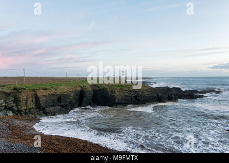 Irish Light House auf einer felsigen Küste mit Wellen bis Ion am Ufer. Stockfoto