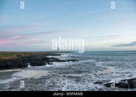 Irish Light House auf einer felsigen Küste mit Wellen bis Ion am Ufer. Stockfoto