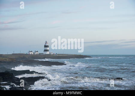 Irish Light House auf einer felsigen Küste mit Wellen bis Ion am Ufer. Stockfoto