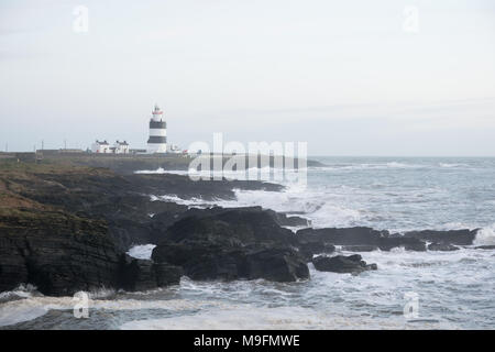 Irish Light House auf einer felsigen Küste mit Wellen bis Ion am Ufer. Stockfoto