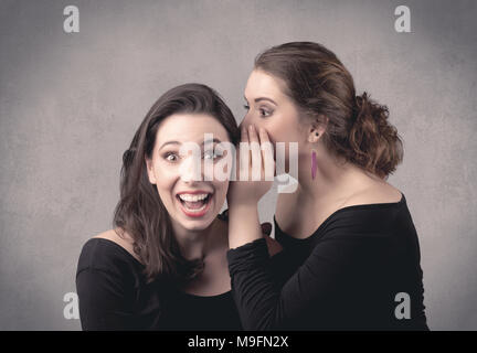 Zwei schick gekleidet Schauspielerin Mädchen mit langem Haar und Make-up Whispering vor Grau im städtischen Hintergrund Konzept. Stockfoto