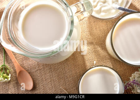Container Milch auf sackleinen Tischdecke mit dekorativen Blumen outdoor in der Natur. Horizontale Komposition. Stockfoto
