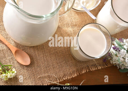Container Milch auf sackleinen Tischdecke mit dekorativen Blumen outdoor in der Natur. Horizontale Komposition. Stockfoto